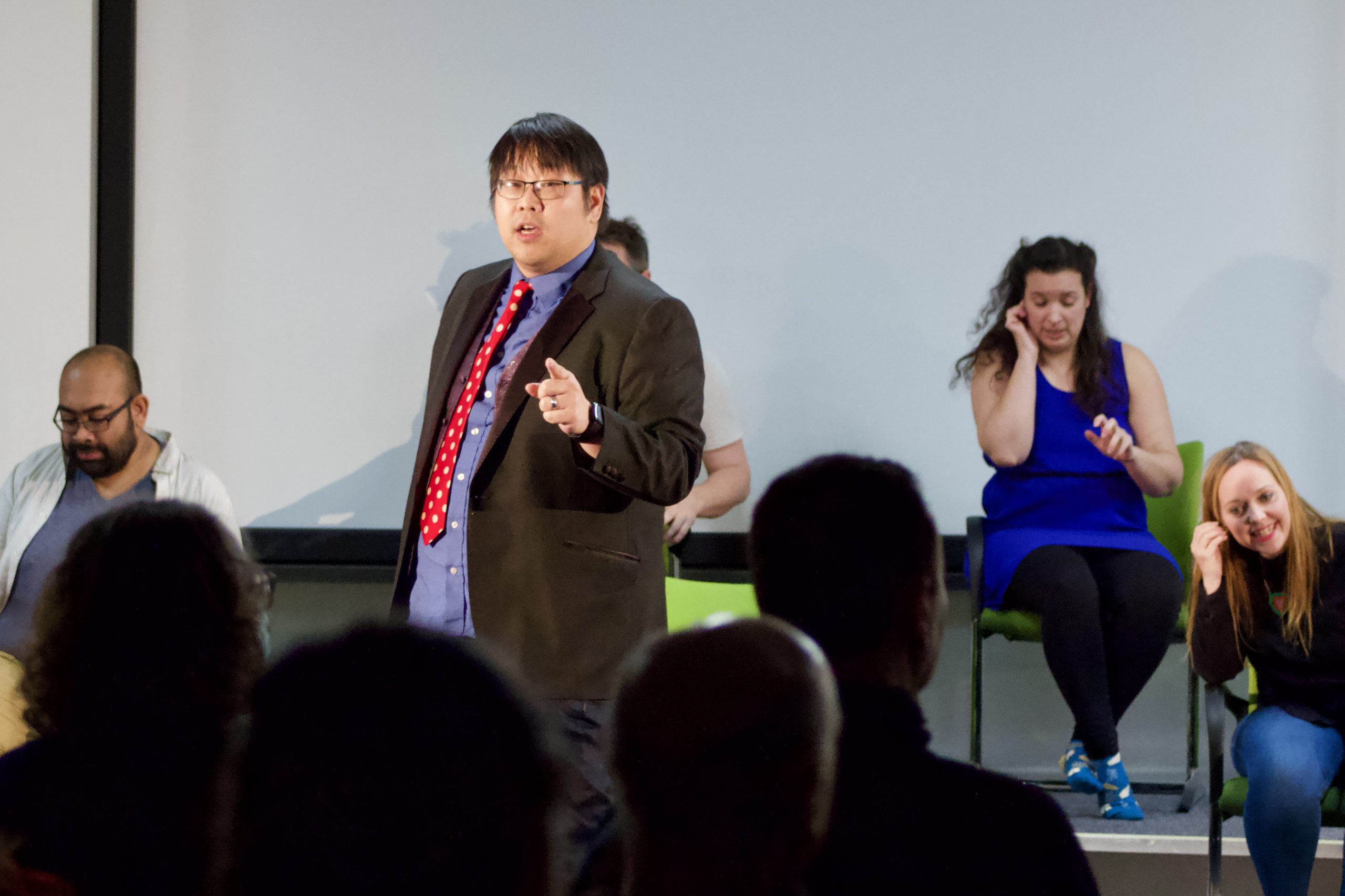 A man in a suit pointing at an audience while talking