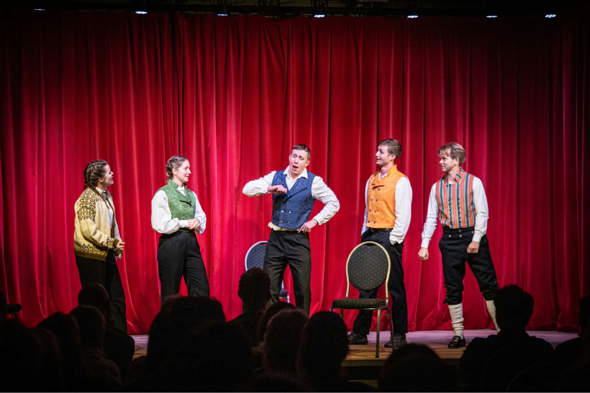 Jon Oslo 3 Five improvisers performing on stage in front of red curtains, with an audience watching