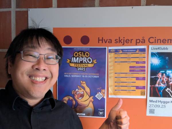 Smiling performer giving a thumbs-up beside a poster for the 2025 Oslo Improv Festival